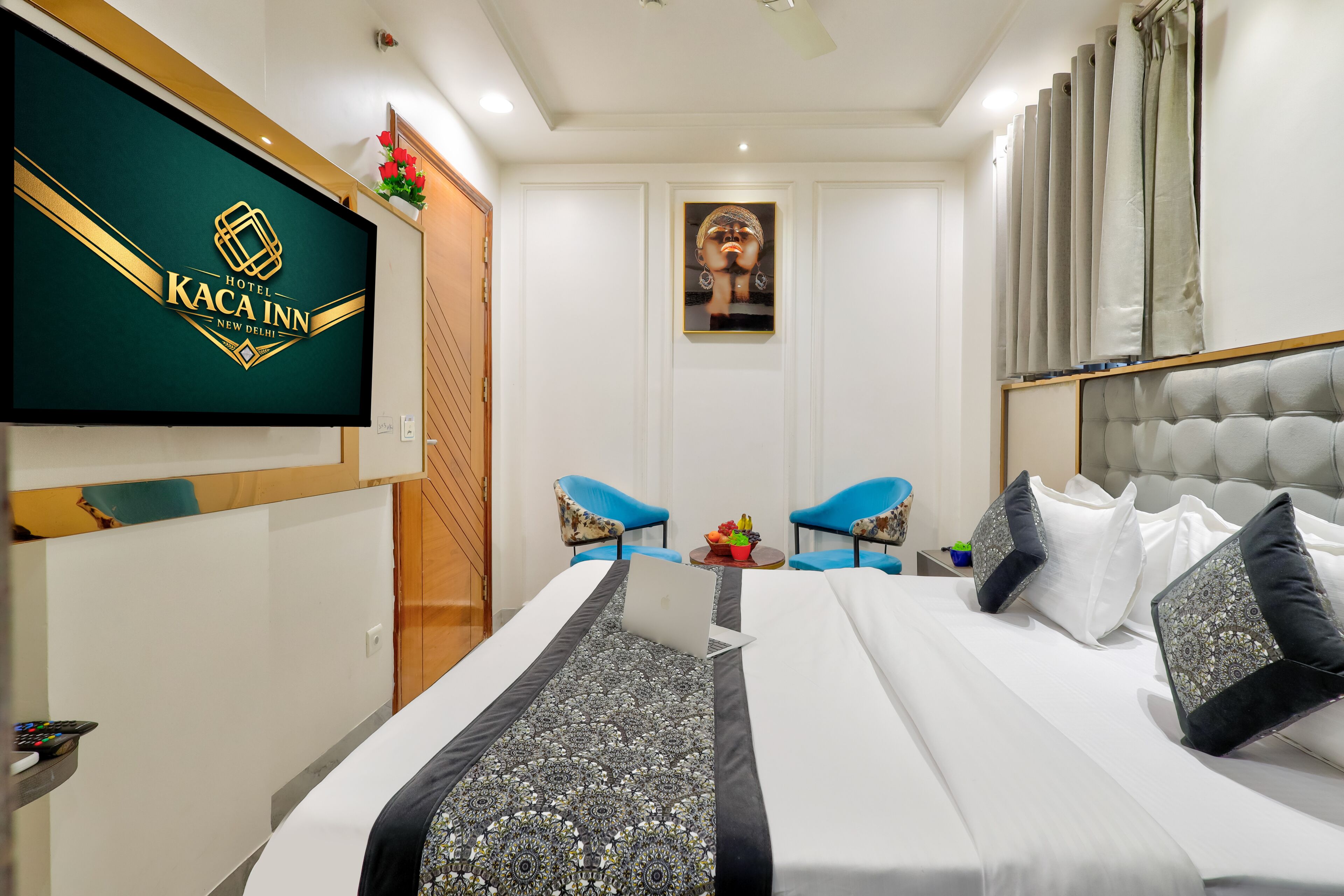 Una habitación de hotel con una cama, dos sillas azules, un televisor y un cuadro en la pared.