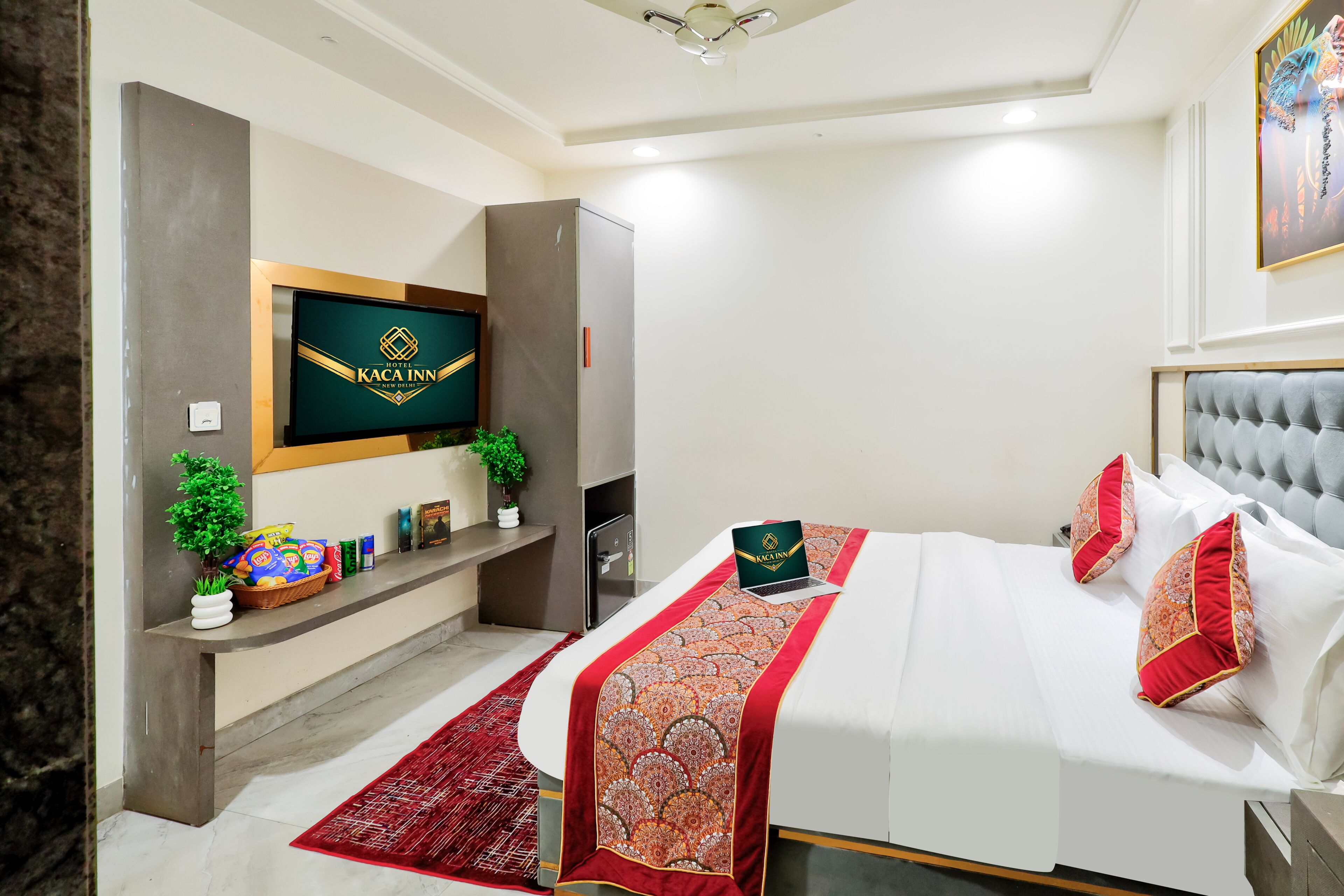 A modern hotel room with a bed, a TV mounted on the wall, a desk with a laptop, and a red rug.