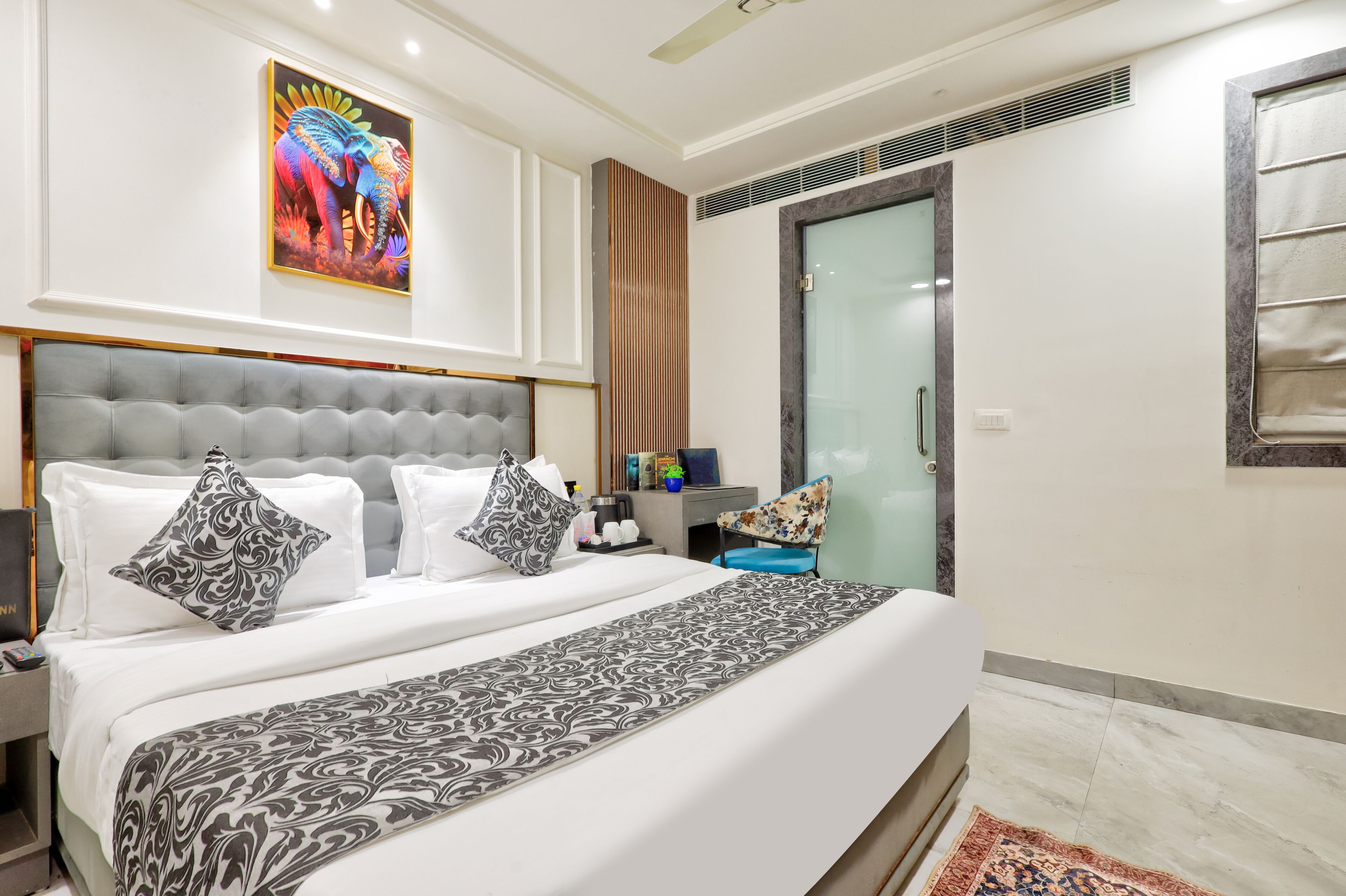 A hotel room with a large bed, a nightstand, a chair, a painting, and a door.