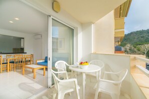 A balcony with a dining area, a white table with chairs, and a bowl of fruit. - Massanet (1a) - Apartment In Canyamel. Free Wifi (Canyamel, Illes Balears)