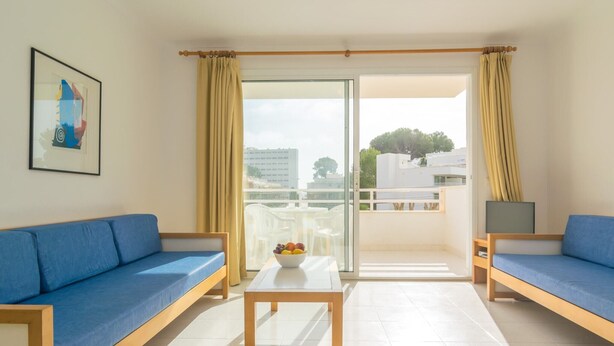 A modern living room with two blue sofas, a wooden coffee table, and a glass door leading to a balcony with outdoor furniture. - Massanet (1b) - Apartment In Canyamel. Free Wifi (Canyamel, Illes Balears)