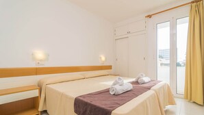 A hotel room with a bed, a bench, a wardrobe, and a sliding glass door to the balcony. - Massanet (1b) - Apartment In Canyamel. Free Wifi (Canyamel, Illes Balears)