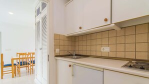 A kitchen with white cabinets, a sink, and a stove. There is a dining area with wooden chairs and a table. - Massanet (1b) - Apartment In Canyamel. Free Wifi (Canyamel, Illes Balears)