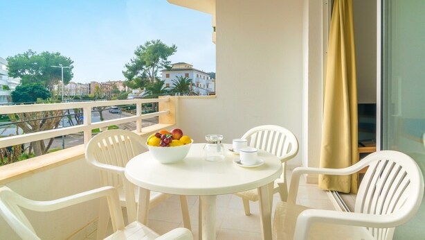 A balcony with a round table, white plastic chairs, a bowl of fruit, and a small table with cups and a glass. - Massanet (1c) - Apartment In Canyamel. Free Wifi (Canyamel, Illes Balears)
