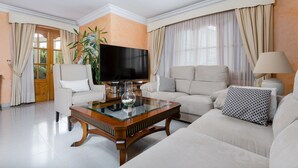 Un salón amplio con una televisión de pantalla plana, una mesa de centro de cristal y un conjunto de sofás.