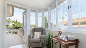 Una habitación con un ventanal grande, un sillón gris, una planta en maceta y una mesa con adornos.