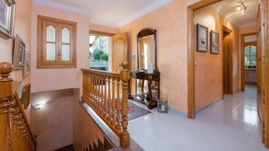 Un pasillo amplio con escalera de madera, un espejo y cuadros en las paredes.
