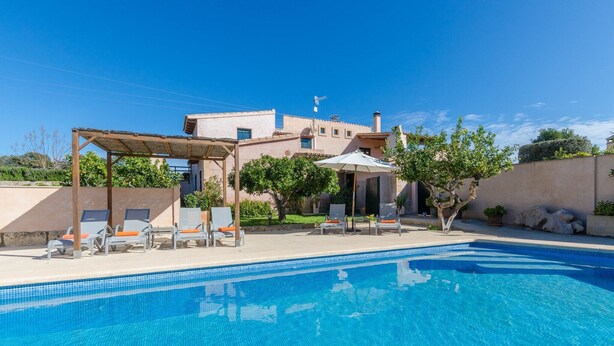 A clear blue swimming pool with lounge chairs and a pergola, surrounded by a landscaped garden and a building in the background. - Pula ViÑas - Villa With Private Pool. Free Wifi (Son Servera, Illes Balears)