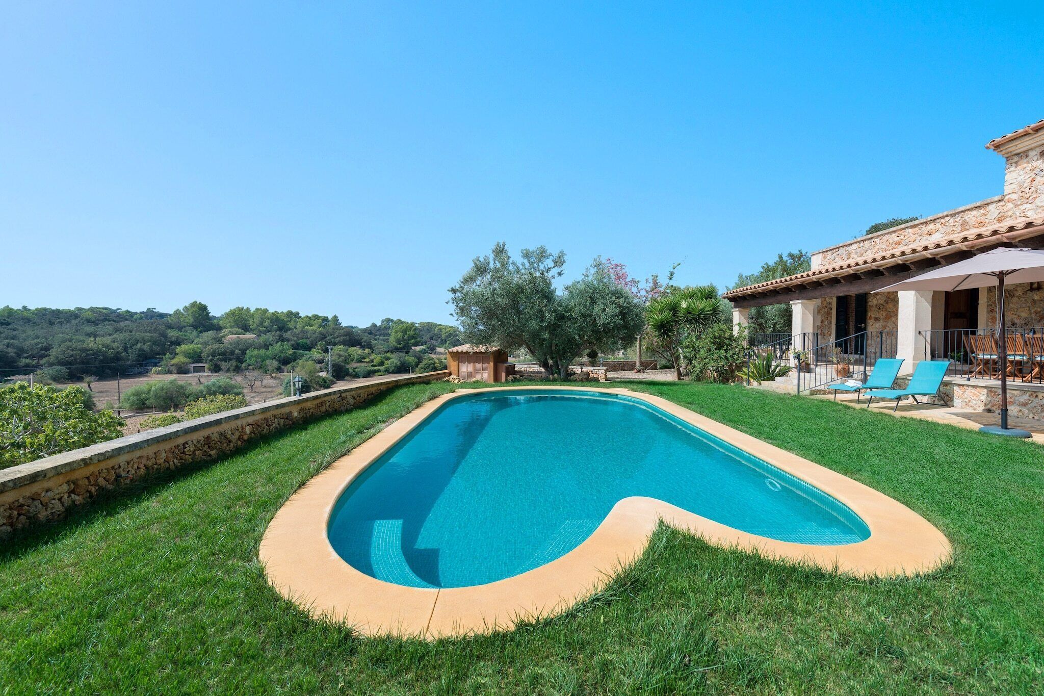 A swimming pool with a stone border, surrounded by a well-maintained lawn and a stone wall.