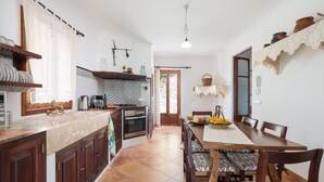 A kitchen with wooden cabinets, a marble countertop, and a dining area with a large table and chairs. - Es Cocons - Villa With Private Pool In Sineu (Sineu, Illes Balears)