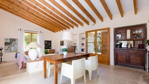 A spacious kitchen with wooden beams, a dining table with chairs, and a cabinet with glass doors.