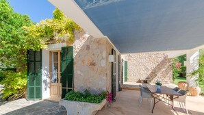 A patio area with a stone wall, green shutters, a table with chairs, and potted plants.