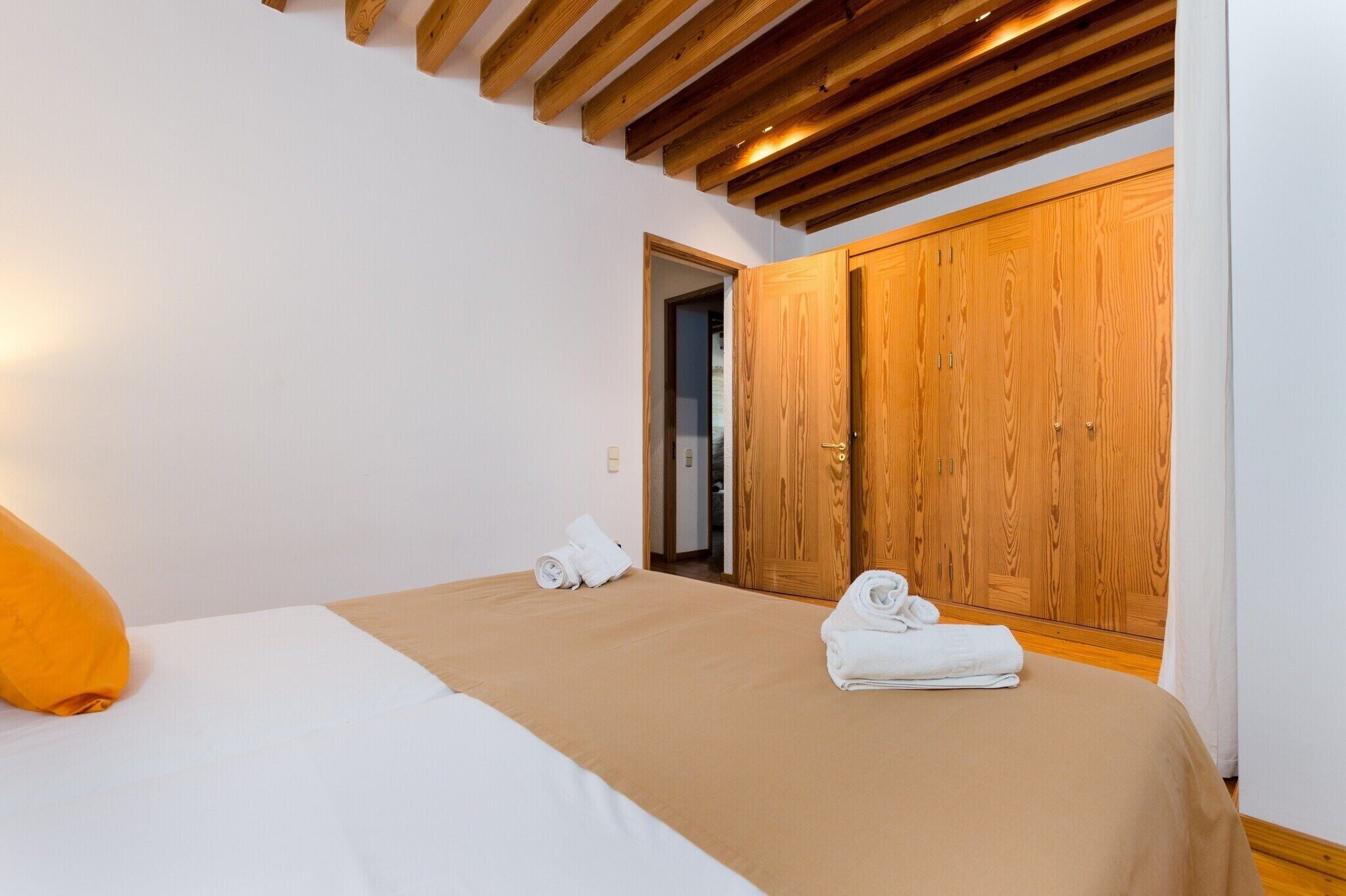 A bedroom with a bed, wooden wardrobe, and a door leading to another room.