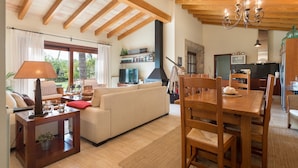 A spacious living room with a sofa, a wooden dining table, and a kitchen area in the background. - Finca Pou Nou - Villa With Private Pool In Inca (Inca, Illes Balears)