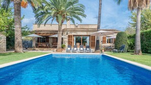 A swimming pool with lounge chairs and umbrellas, surrounded by palm trees and a stone building with a tiled roof. - Finca Pou Nou - Villa With Private Pool In Inca (Inca, Illes Balears)