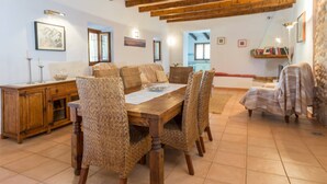 A dining area with a wooden table and wicker chairs, a wooden cabinet, and a stone wall.