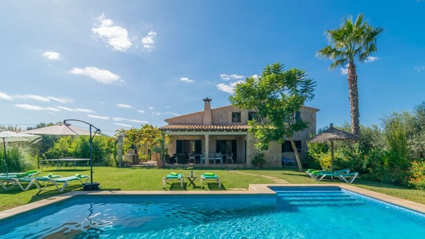 A swimming pool with lounge chairs, a patio area, and a house with a tiled roof and palm trees. - Mercader - Villa With Private Pool In Alcúdia (Alcúdia, Illes Balears)