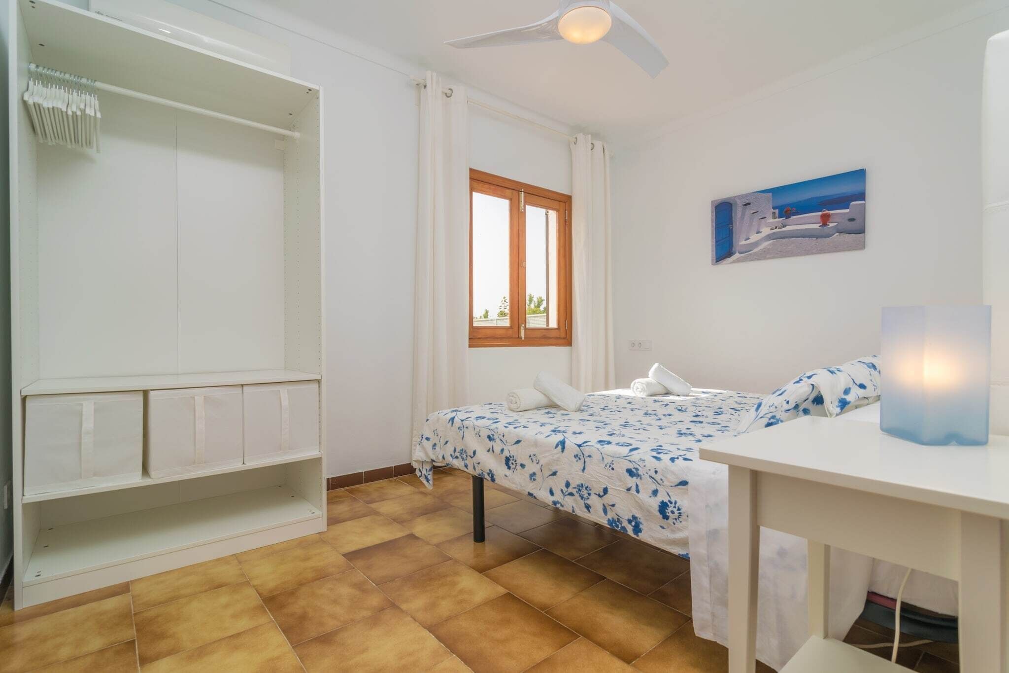 Een slaapkamer met een bed, een kledingkast, een raam en een plafondventilator.