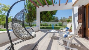 A patio with a hanging chair, a rocking chair, and a small table with a vase.
