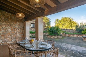 An outdoor dining area with stone walls, wicker chairs, and a stone table set for a meal. - N'amera - Villa With Private Pool In Campos (Campos, Illes Balears)