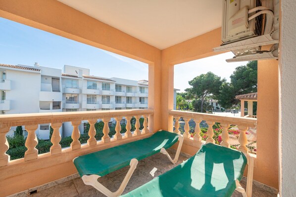 A balcony with a green cushioned seating area, beige balustrades, and a view of white buildings and trees.