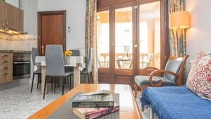 Une pièce confortable comprenant un lit, une table en bois avec des livres, un coin repas avec des chaises et une cuisine équipée de placards et d’une cuisinière.