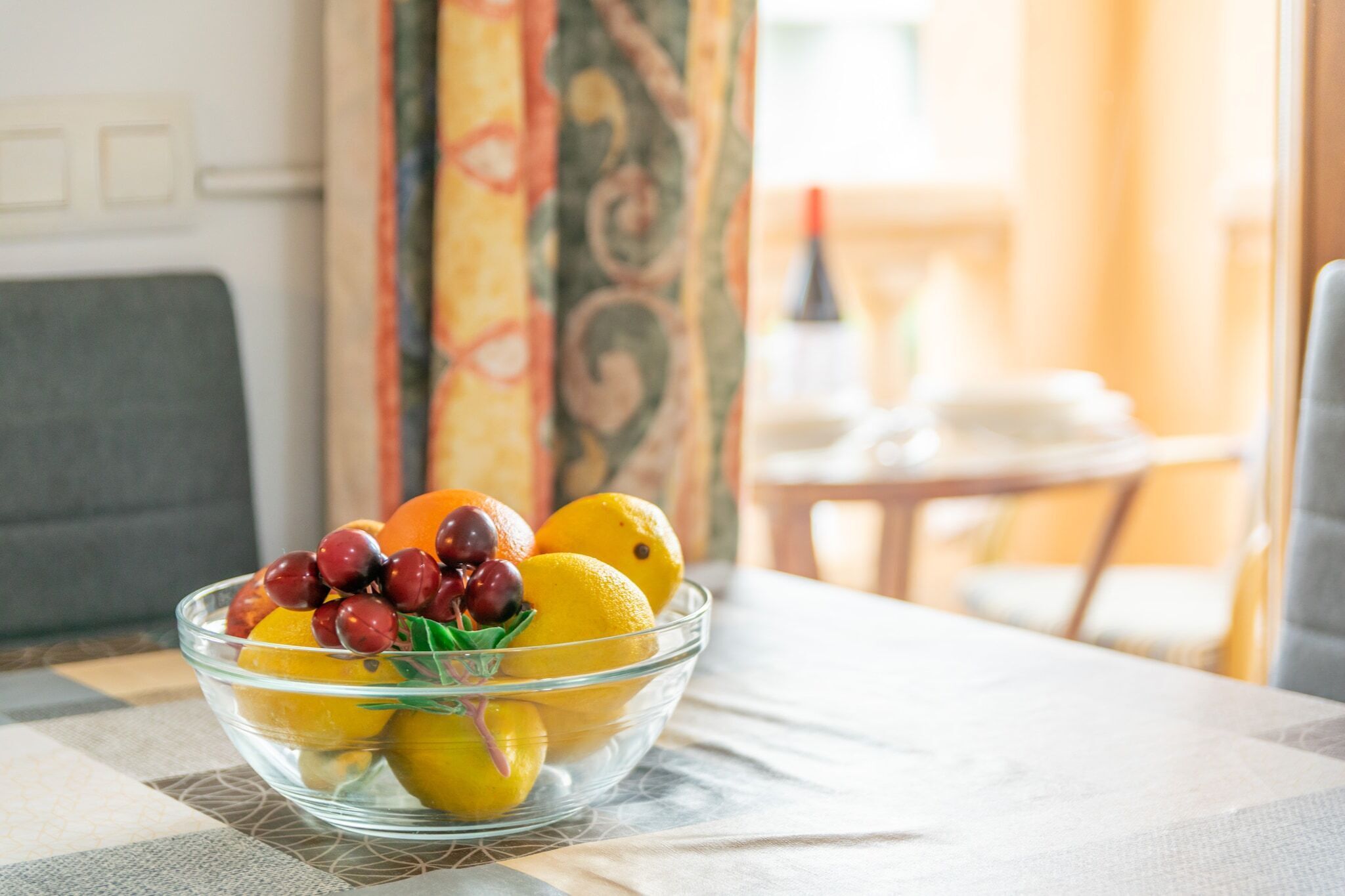 Un bol de vidrio transparente lleno de limones, naranjas y uvas sobre una mesa.