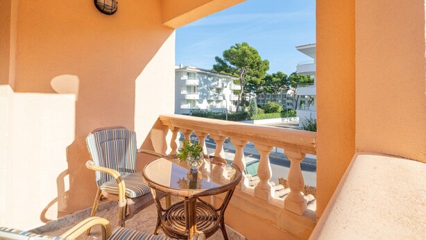 Un balcon avec une table ronde, une chaise à rayures et un pot de fleurs.