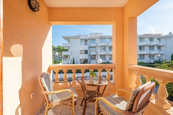 A balcony with wicker chairs, a glass table, and a view of multi-story buildings. - Casa Miriam - Apartment In Cala Lliteres (Cala Ratjada, Illes Balears)