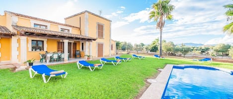 Zona de piscina con piscina, sillas de descanso y un edificio de fachada amarilla.
