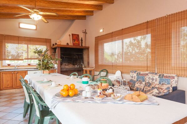 A dining area with a long table set for a meal, surrounded by chairs, and a fireplace in the background. - Ca Na Granada - Villa With Private Pool In Muro (Muro, Illes Balears)