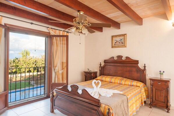 A bedroom with a wooden bed, a ceiling fan, a nightstand, and a view of a swimming pool through a sliding glass door. - Ca Na Granada - Villa With Private Pool In Muro (Muro, Illes Balears)