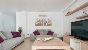 Una sala de estar moderna con un sofá gris, una mesa de centro de madera y un televisor de pantalla plana sobre un mueble de madera.