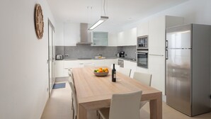 Una cocina moderna con armarios blancos, una mesa de comedor de madera y un refrigerador de acero inoxidable.