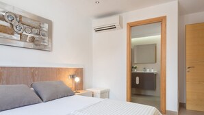 Un dormitorio con cama, mesita de noche, lámpara y aire acondicionado instalado en la pared.