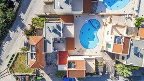 Luftaufnahme eines Wohngebiets mit zwei Schwimmbecken, gefliesen Dachungen und einem kleinen Garten.