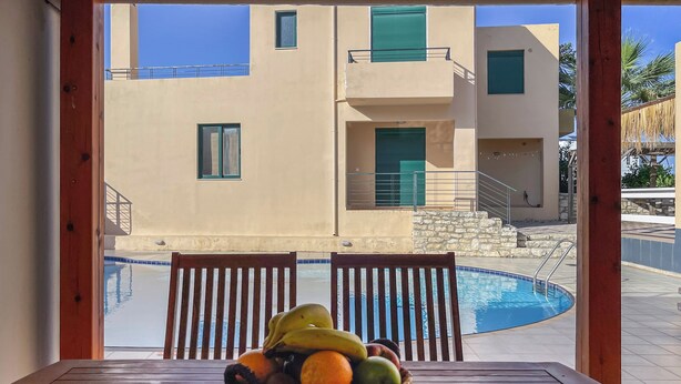 Ein Holztisch mit einer Obstschale in einem Raum mit Blick auf einen Swimmingpool und ein Gebäude mit Balkonen.