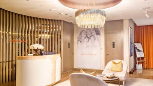 A hotel reception area with a modern design, featuring a reception desk, a chandelier, and a poster of a couple. - LUX Paramount Burj View Business Bay (Dubai)