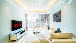 A modern bedroom with a large TV, a bed, a sofa, and a view of the city. - LUX Paramount Burj View Business Bay (Dubai)