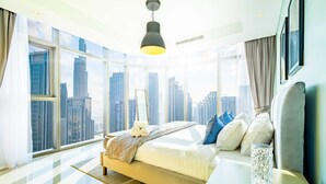 A modern bedroom with a large bed, a bedside table, a mirror, and a view of a cityscape through large windows. - LUX Paramount Burj View Business Bay (Dubai)