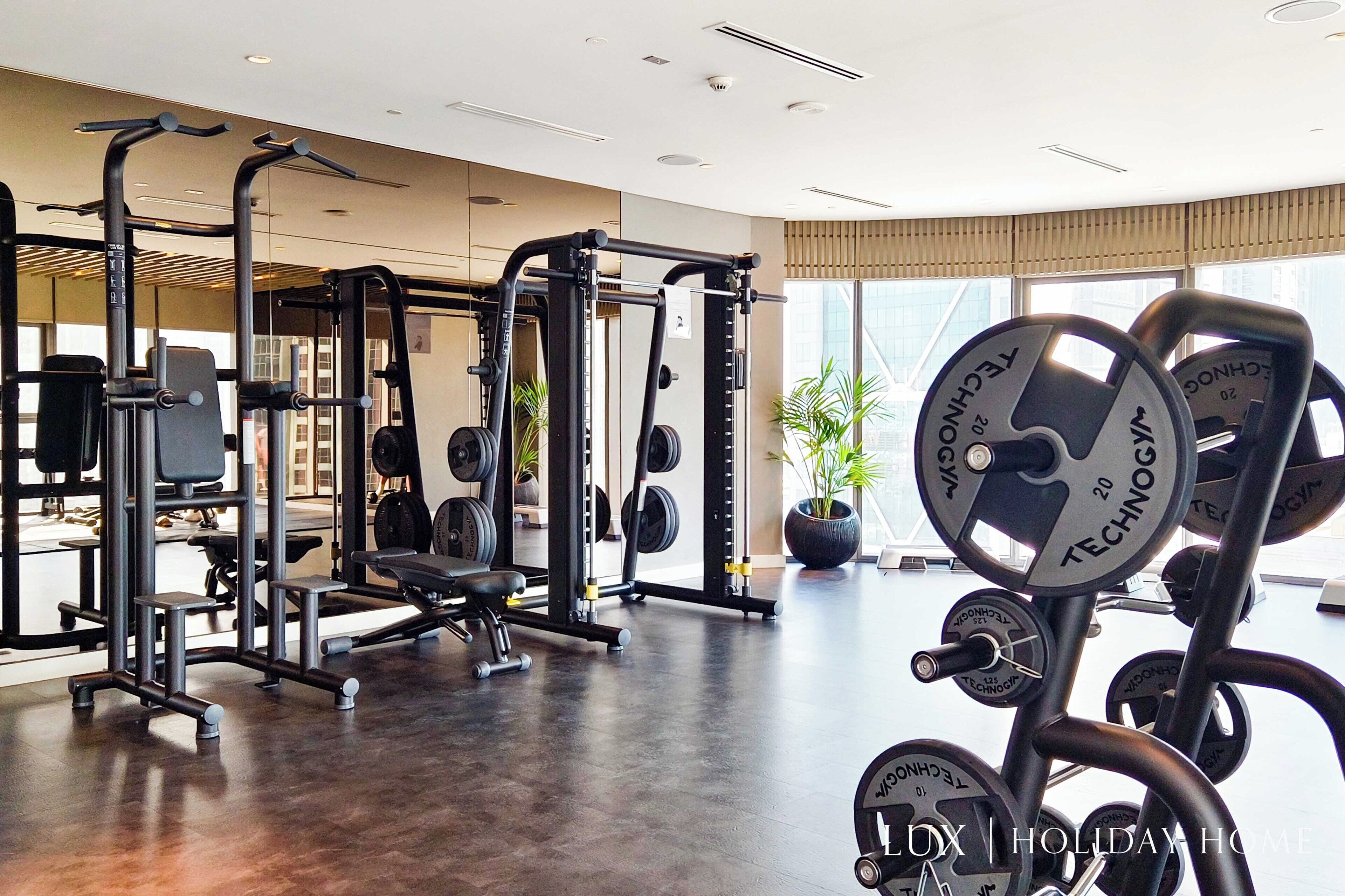 Une salle de sport moderne dotée de divers appareils d’exercice, de grandes fenêtres et d’un intérieur propre et bien éclairé.