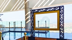 A modern hotel lobby with a large glass window, a pool area, and a view of a Ferris wheel. - LUX Paramount Burj View Business Bay (Dubai)