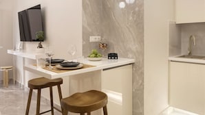 A modern kitchen with a marble backsplash, a built-in island with stools, and a flat-screen TV mounted above the island. - Millerou16-18·Elegant minimal studio in Kerameikos (Athens)