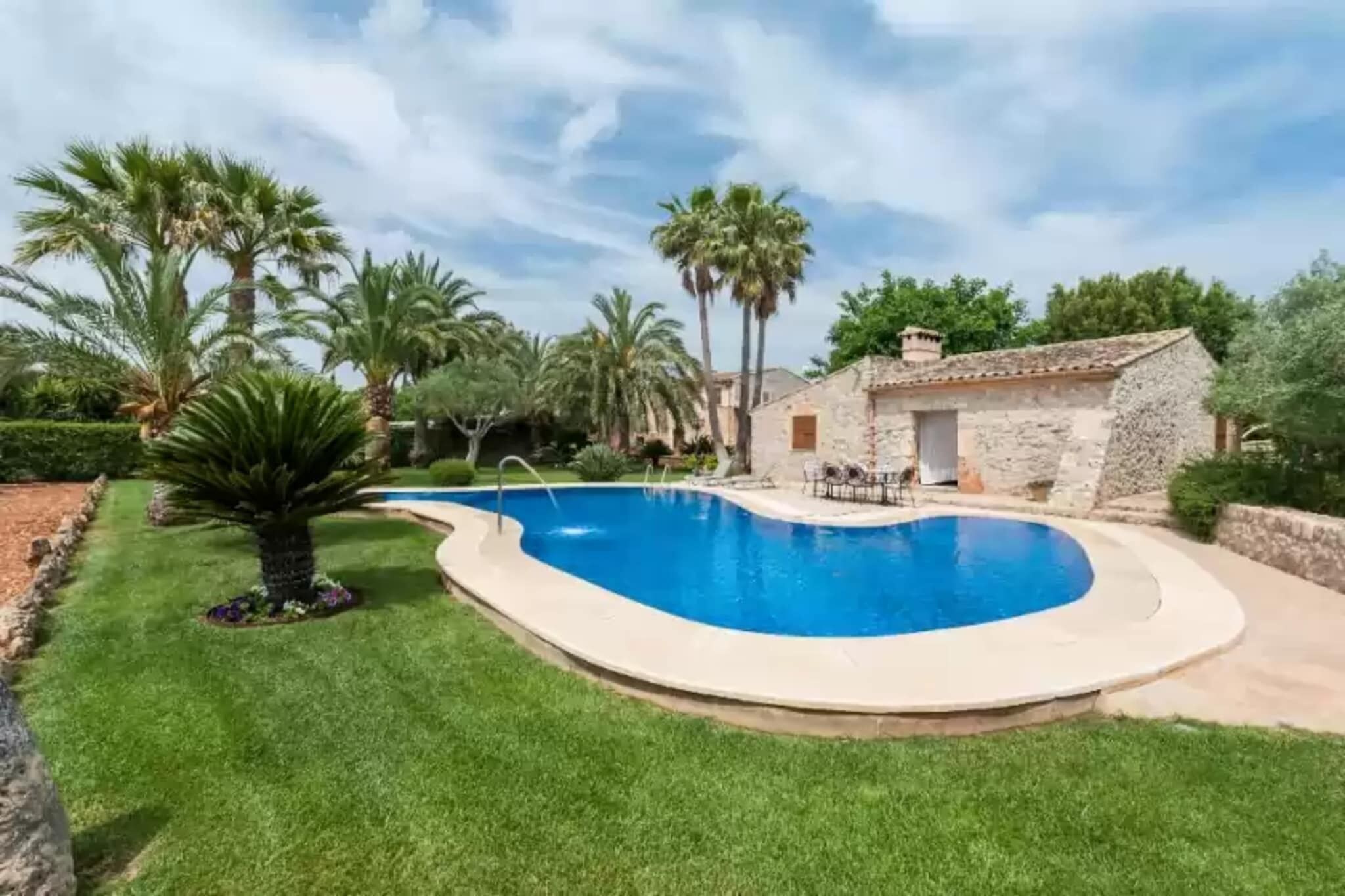 A swimming pool with a stone house and palm trees in the background.