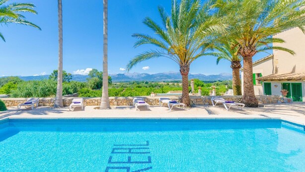 A clear blue pool with lounge chairs and palm trees, surrounded by a stone wall and a view of mountains. - Son Real - Villa With Private Pool In Sencelles (Sencelles, Illes Balears)