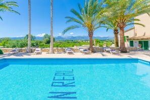 A clear blue pool with lounge chairs and palm trees, surrounded by a stone wall and a view of mountains. - Son Real - Villa With Private Pool In Sencelles (Sencelles, Illes Balears)