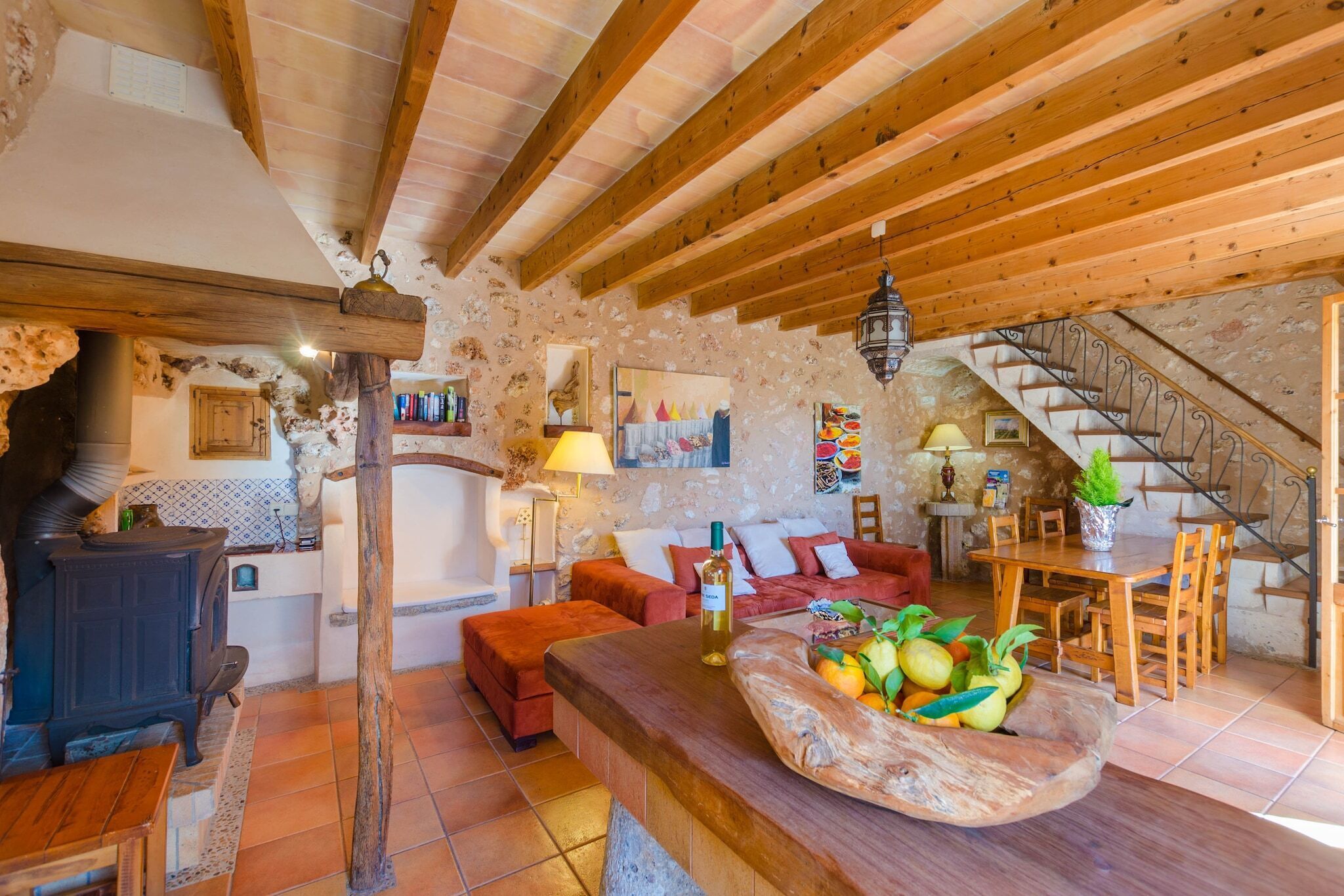 Un interior rústico con vigas de madera a la vista, pared de piedra, mesa de comedor de madera y una escalera.