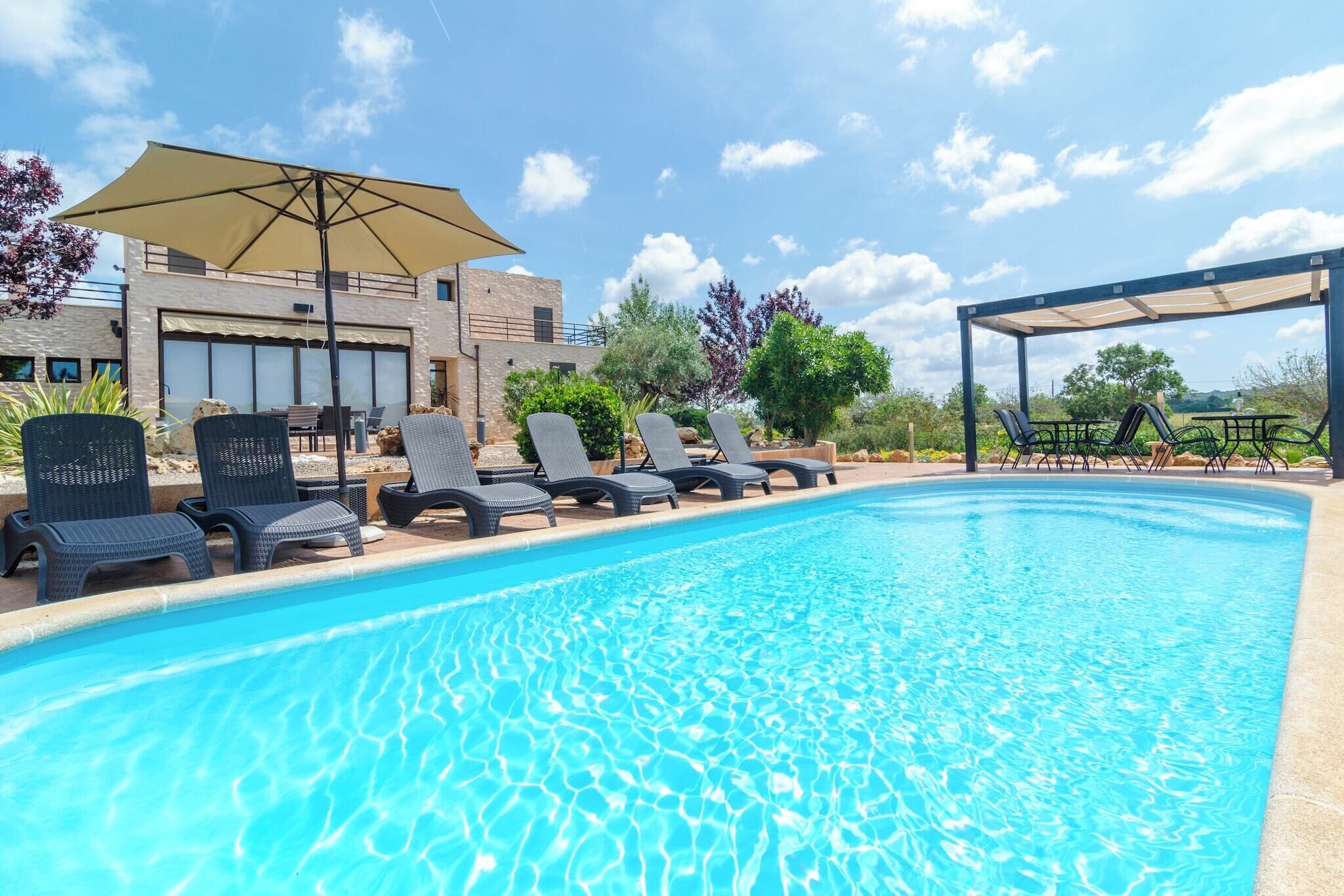 A swimming pool with lounge chairs and umbrellas, surrounded by a building with large windows and a covered area.