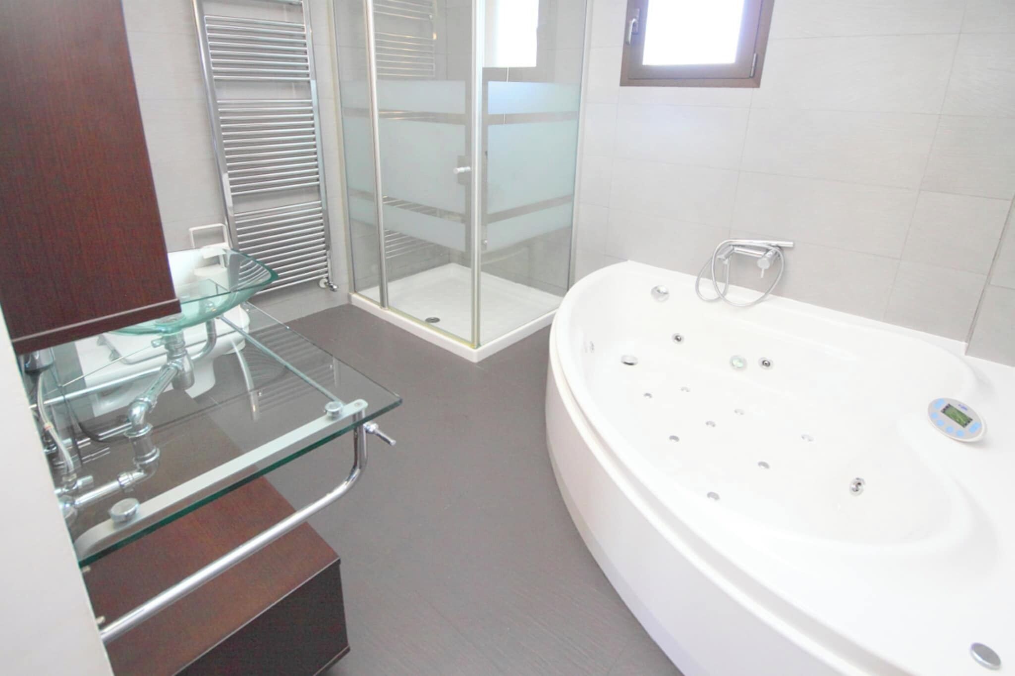 Un bagno moderno con cabina doccia in vetro, una vasca freestanding e un mobile vanitario con piano in vetro.