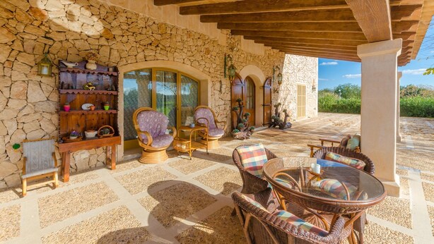 A covered patio area with stone walls, wicker furniture, and a stone floor.
